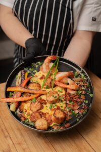Scallops and shrimp plated with bacon and vegetables being served